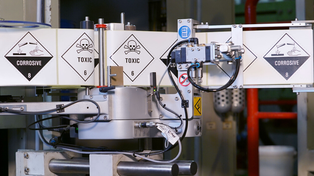 Label applicator applying hazardous labels on chemical products
